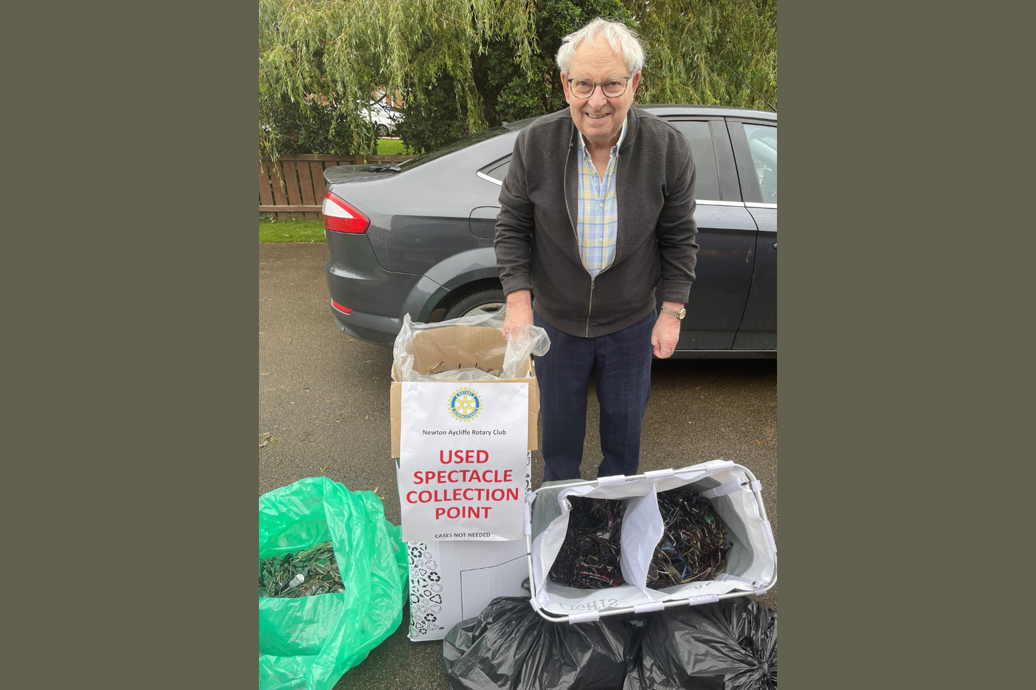 Geoff Batchelor standing with bags of used spectacles he has collected