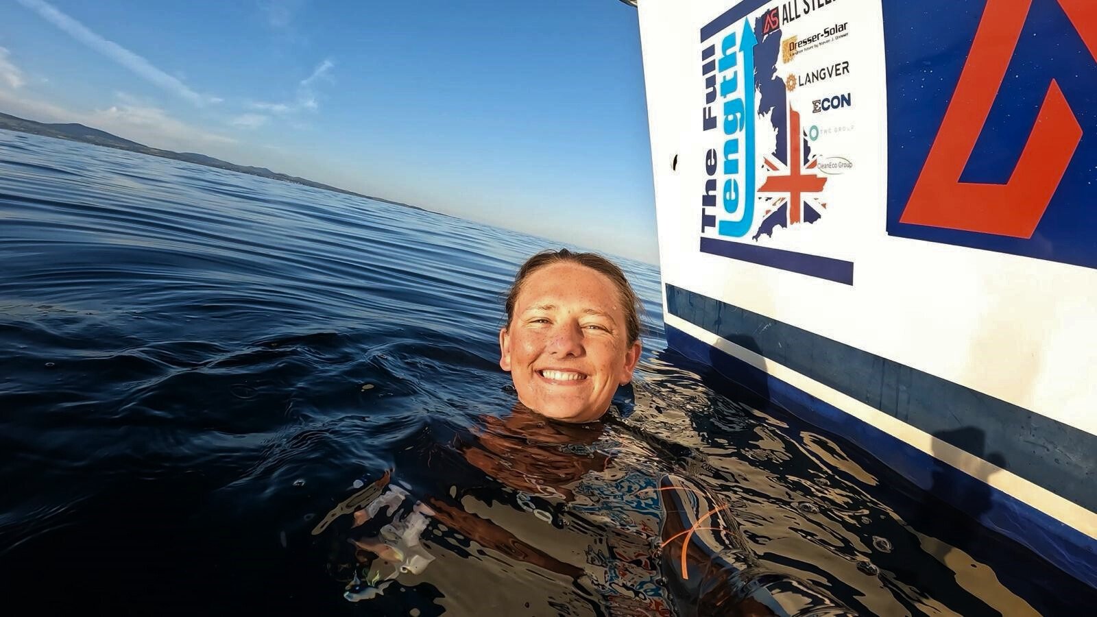 A person is smiling in the water next to a boat