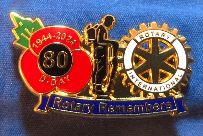 a badge with the words rotary remembers on it, a red poppy, Rotary logo and silhouette of a soldier