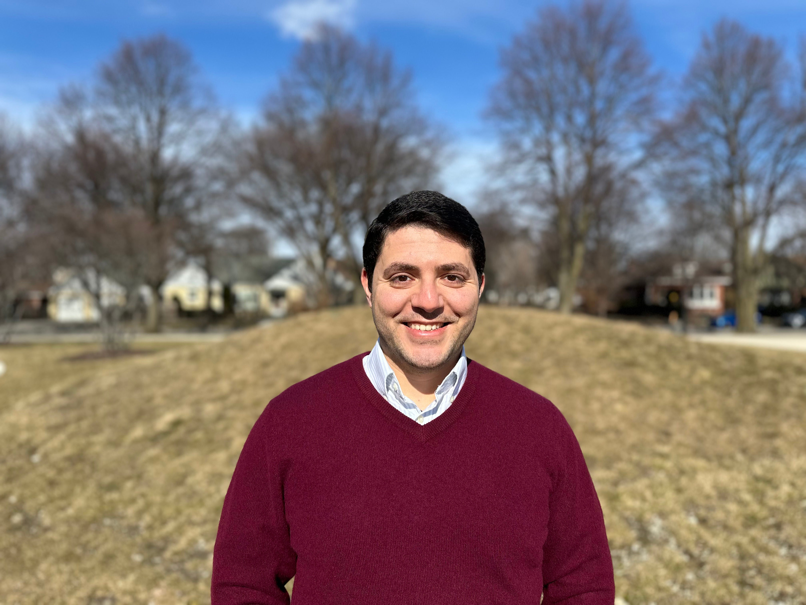 Mohammed Eid in a red sweater standing in front of a grassy field