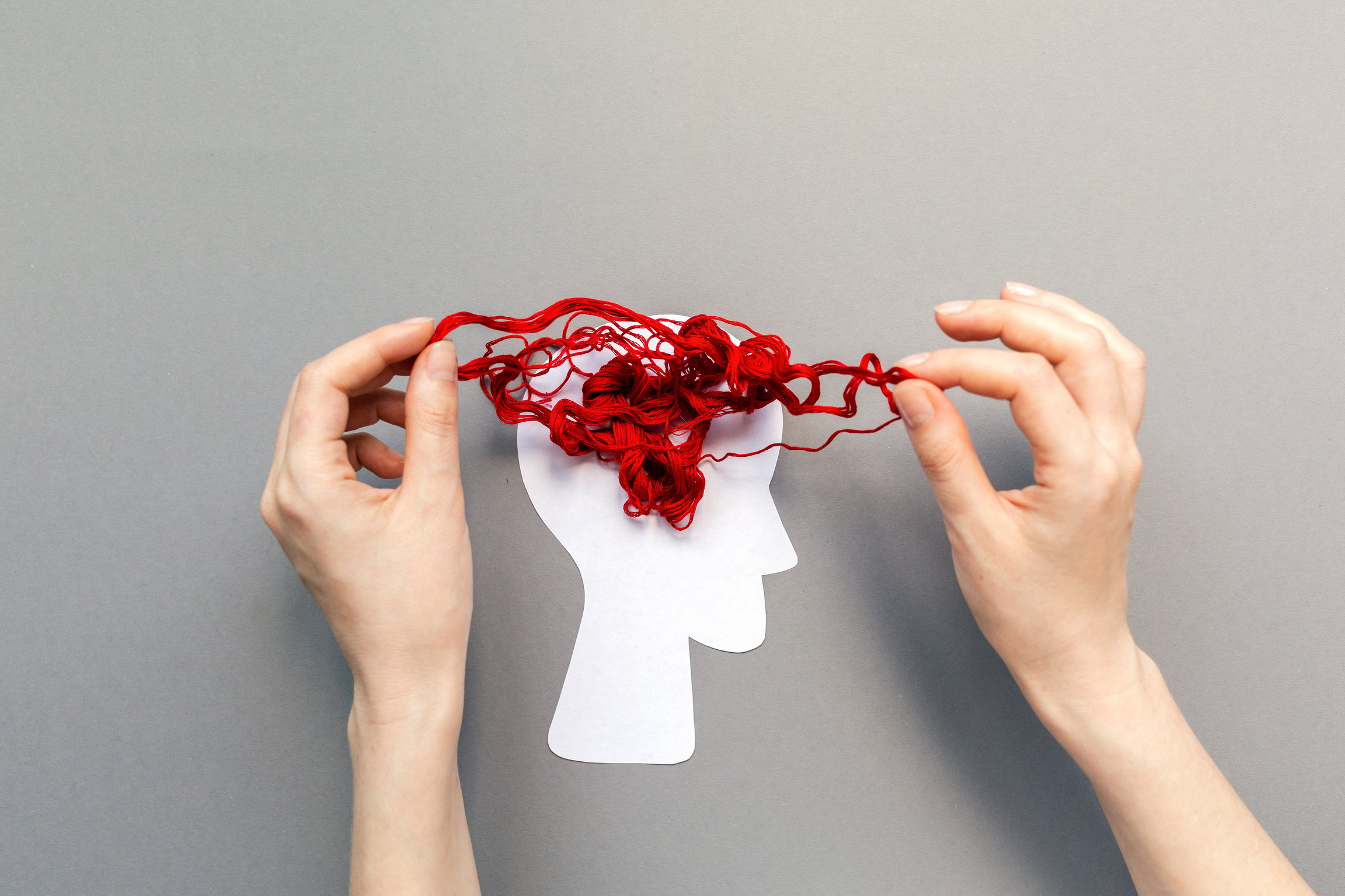 two hands holding a paper cutout of a human head with red string tied in knots