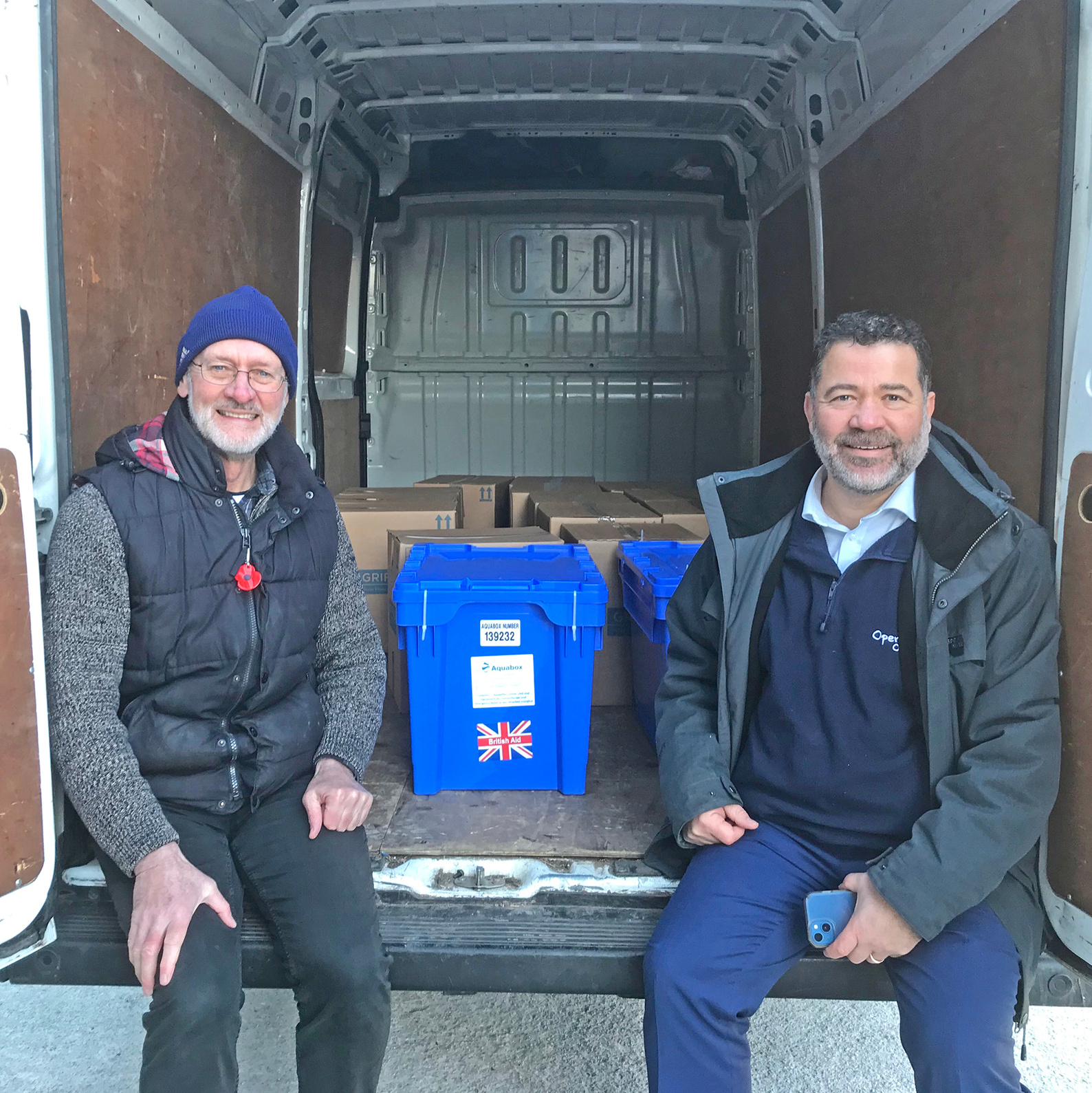 two people sitting next to each other in the back of a truck containing boxes of water filters