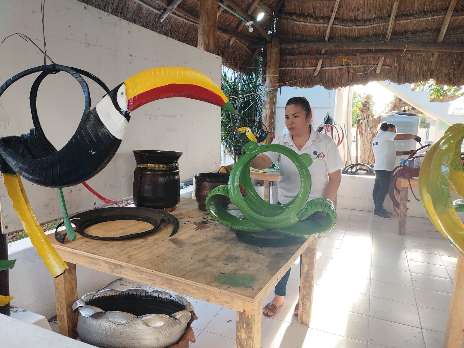 a woman in an outdoor workshop paints tyres that have been reworked into animal shapes.