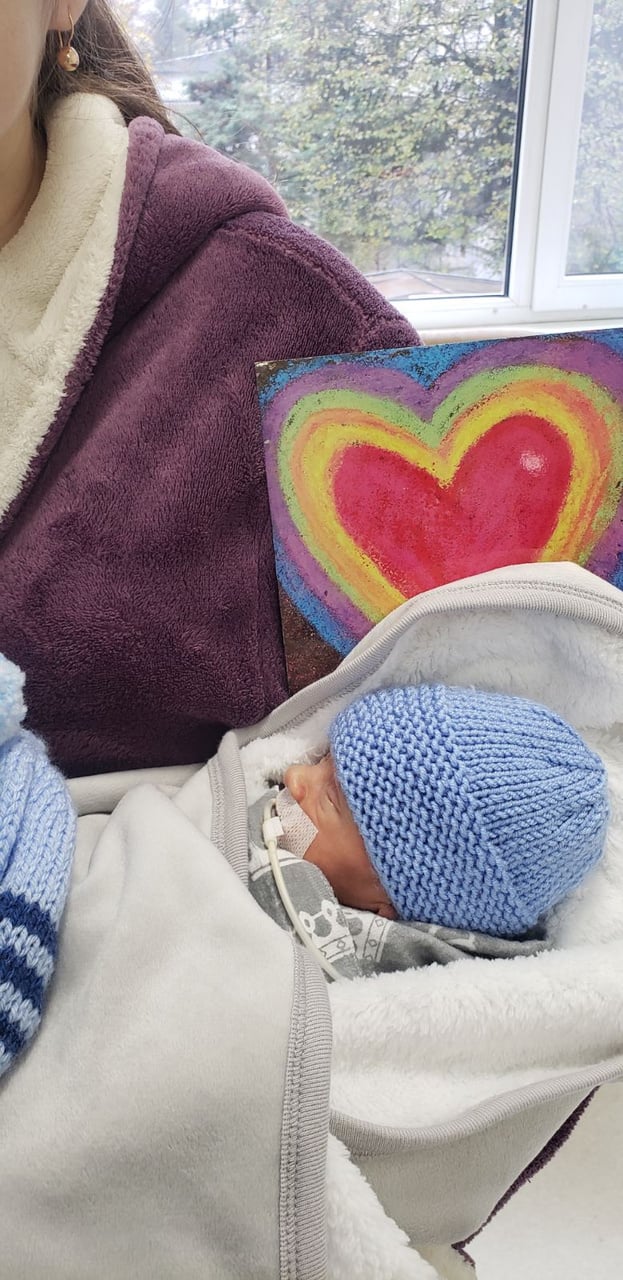 A baby in a blanket with a blue knitted hat.