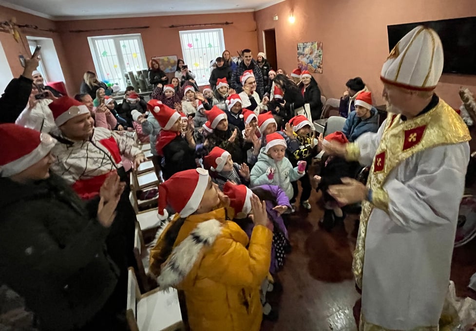 A Rotarian dressed as Saint Nicholas in a room of Ukrainian children wearing Santa hats.