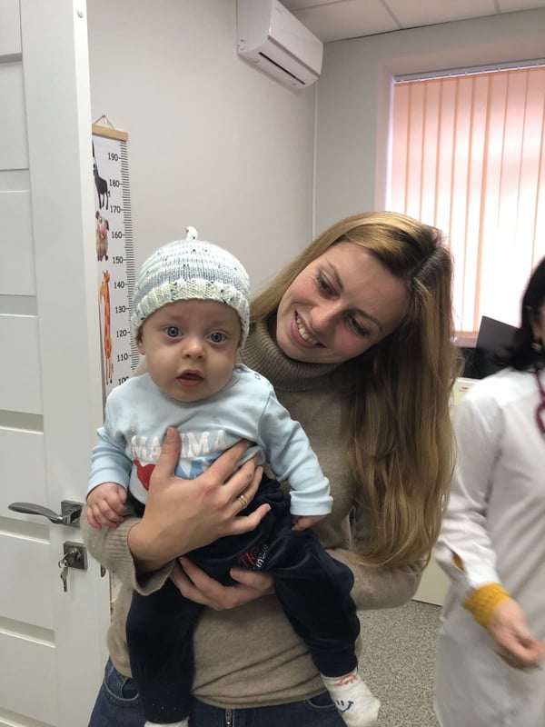 A woman holding a baby wearing a knitted hat in a doctor's office.