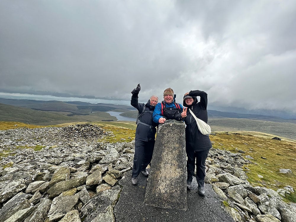 three people pose for a picture on top of a mountain