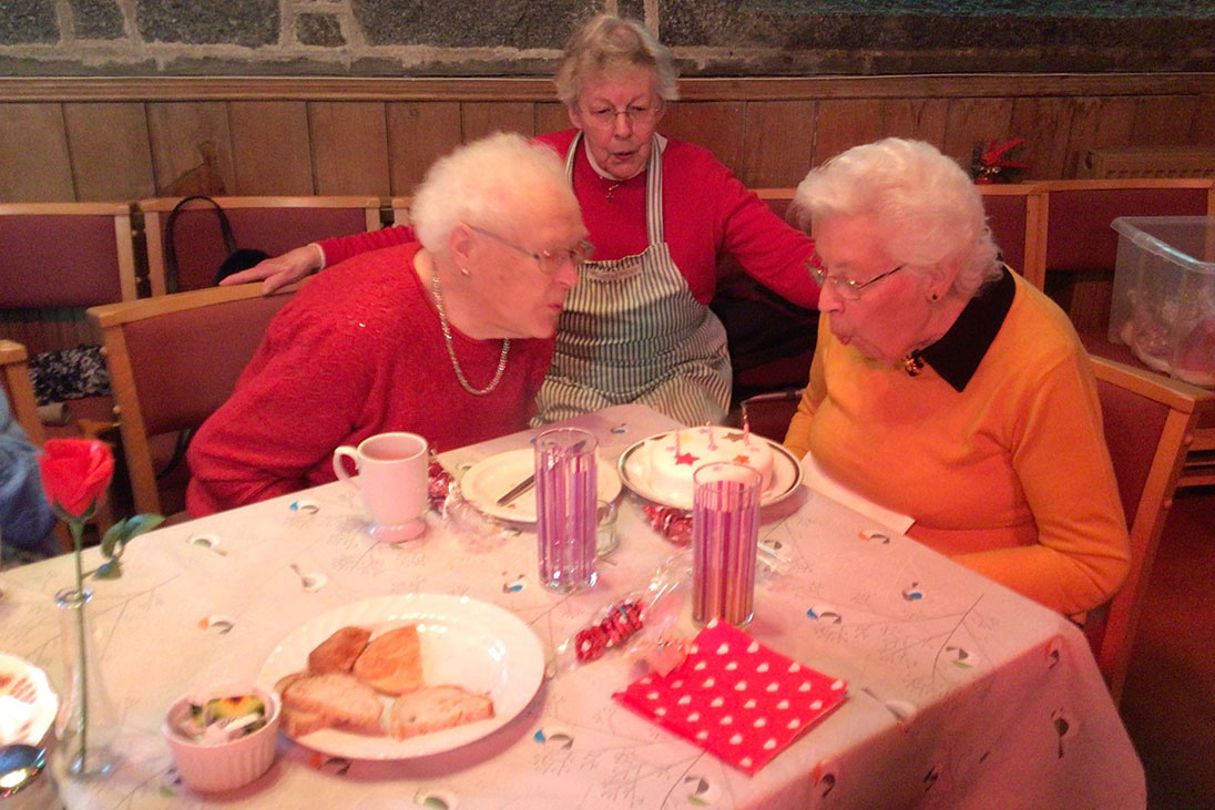 a group of elderly people sitting at a table blowing out candles on a cake