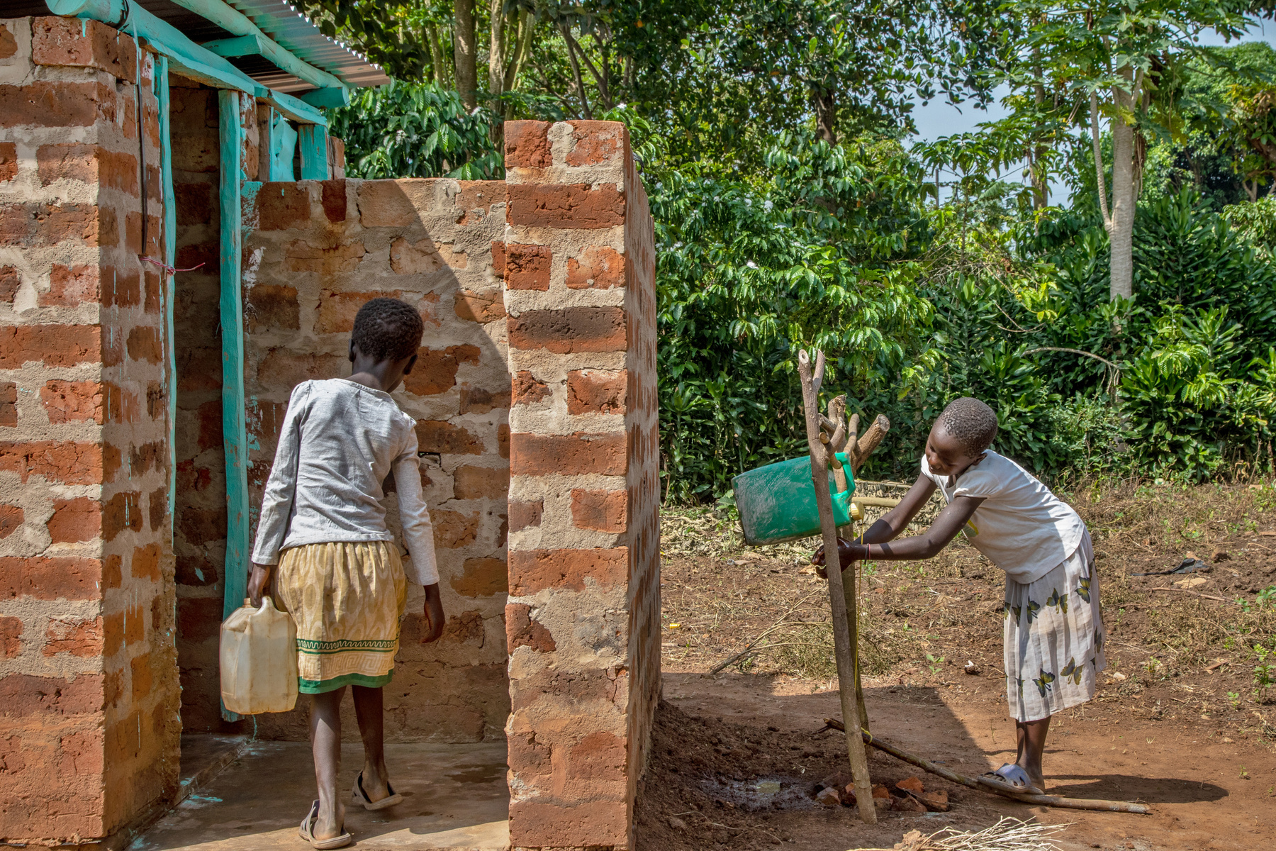 two children are standing in front of a brick building accessing clean water from a well