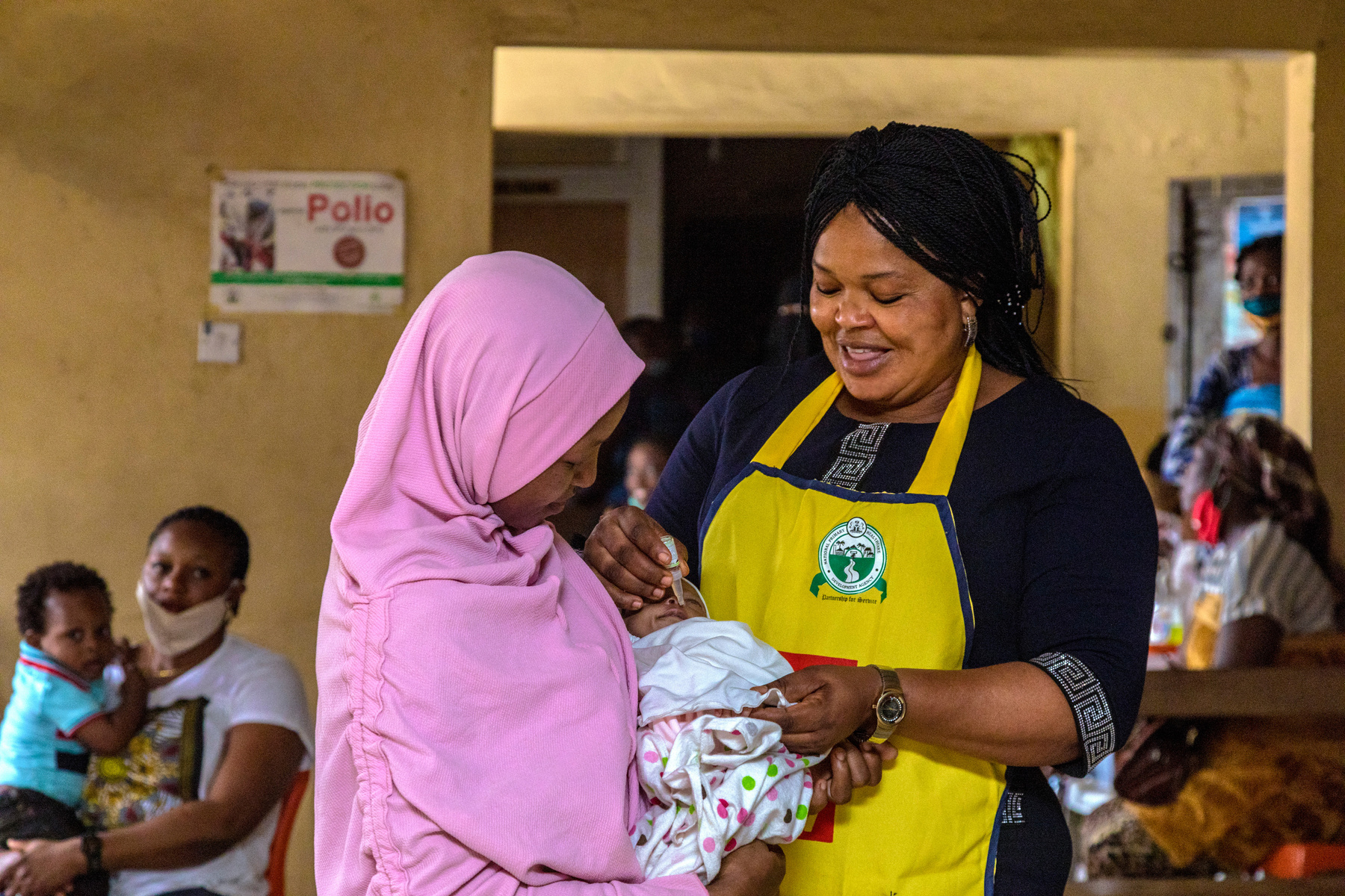 a person in a yellow apron giving a baby a polio vaccine